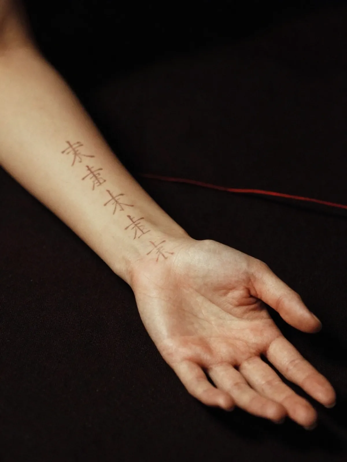 A woman's forearm with faint Heavenly Stem characters traced from wrist to elbow
