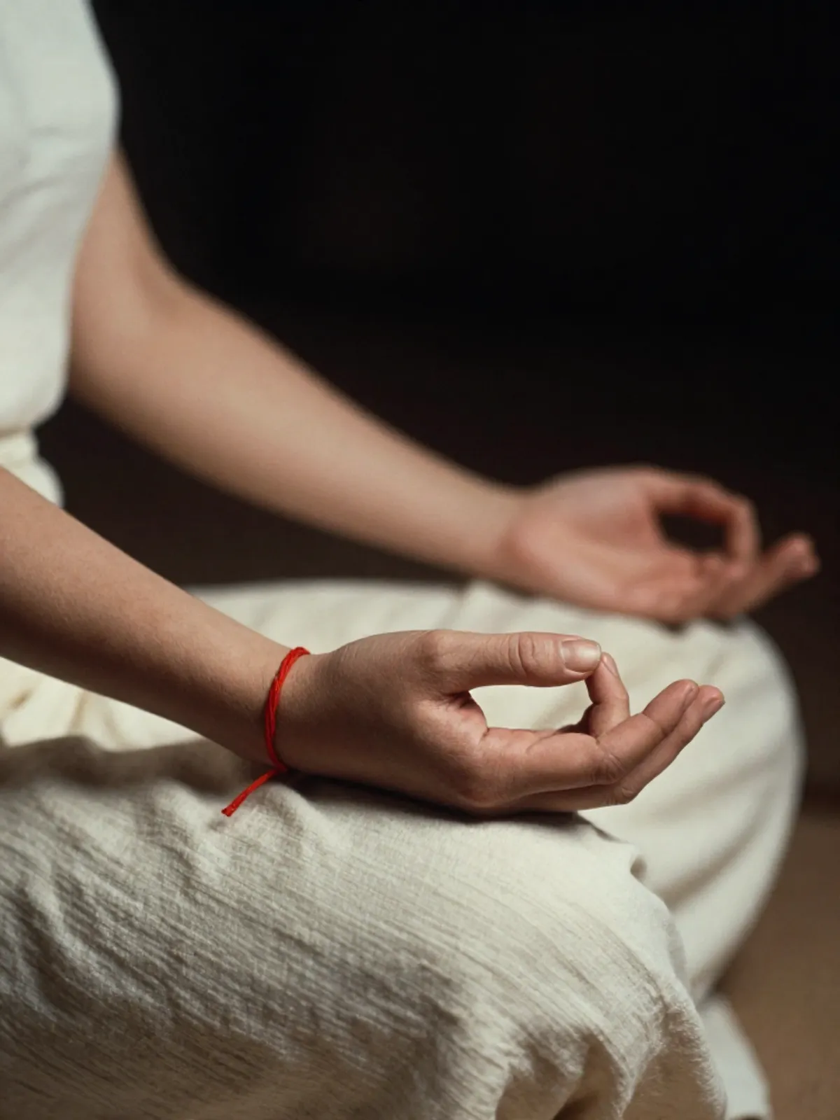 A woman's hands in meditation mudra, a crimson thread on her wrist