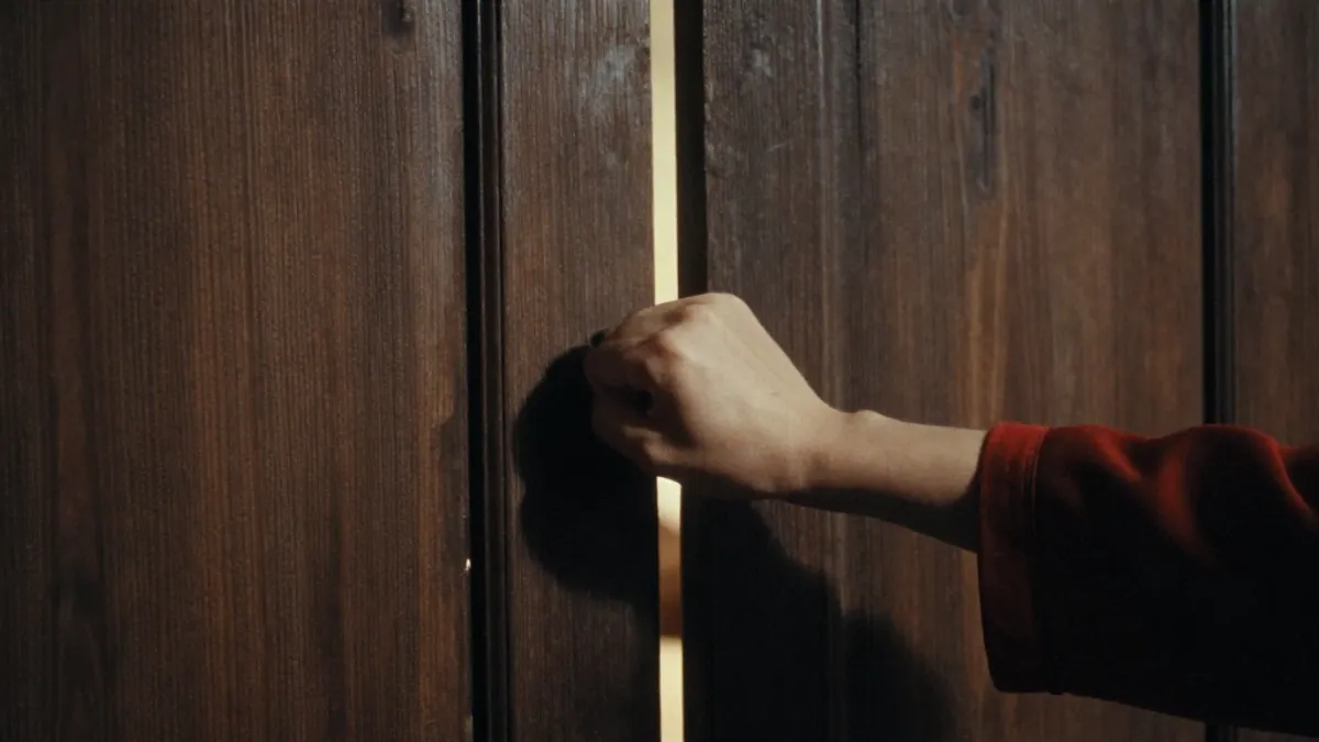 A fist knocking on a wooden door at night, lamplight beneath